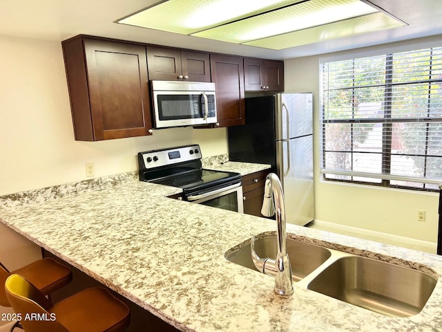 kitchen featuring light stone countertops, dark brown cabinets, stainless steel appliances, and sink