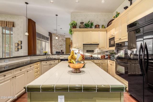 kitchen with black appliances, tile countertops, a kitchen island, and pendant lighting