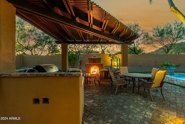 patio terrace at dusk with an outdoor kitchen, exterior fireplace, and a grill