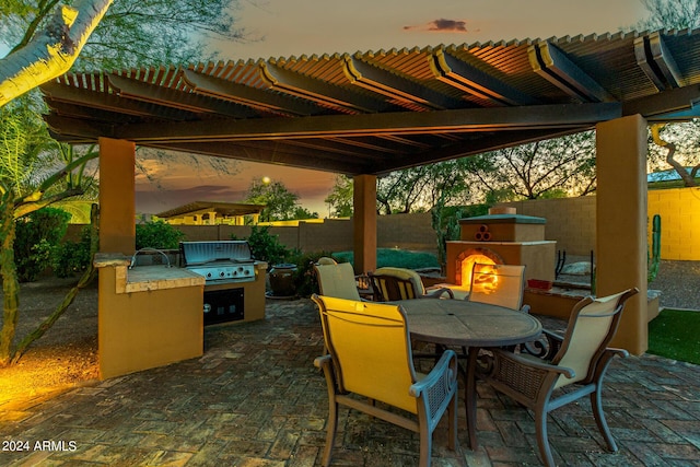 patio terrace at dusk featuring area for grilling, a grill, and exterior fireplace