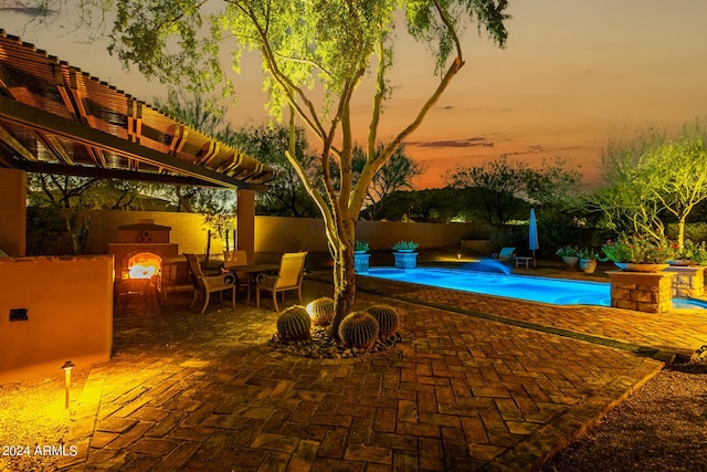 pool at dusk featuring an outdoor fireplace and a patio