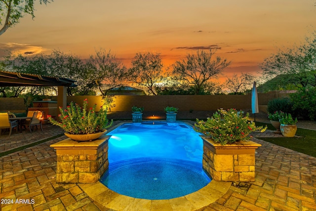 pool at dusk featuring a patio and a hot tub