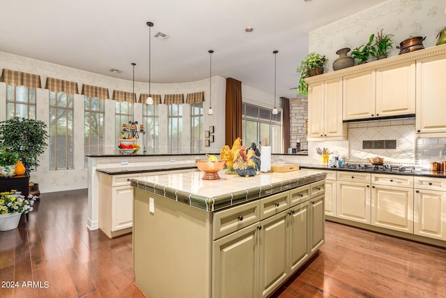 kitchen with stainless steel gas stovetop, decorative light fixtures, hardwood / wood-style floors, a kitchen island, and tile counters