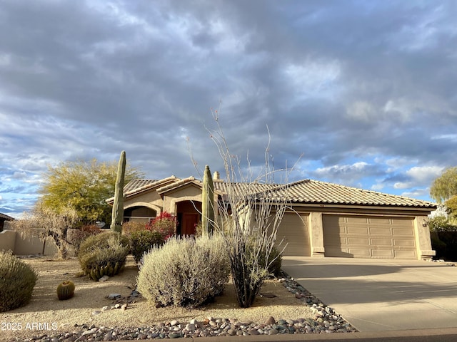 view of front of house with a tiled roof, an attached garage, driveway, and stucco siding