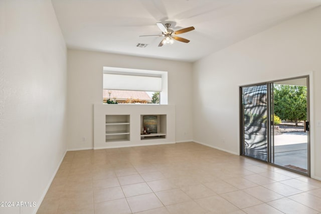 unfurnished living room featuring built in shelves, ceiling fan, light tile patterned floors, and a healthy amount of sunlight