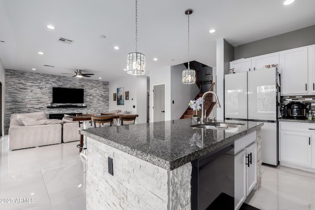 kitchen featuring dark stone counters, decorative light fixtures, an island with sink, and white cabinets