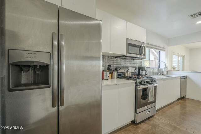 kitchen featuring sink, concrete floors, white cabinets, stainless steel appliances, and backsplash