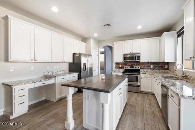 kitchen with appliances with stainless steel finishes, light wood-type flooring, white cabinetry, and a kitchen island