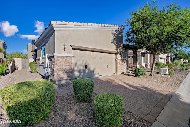 view of front facade with a garage, central AC, stone siding, decorative driveway, and stucco siding