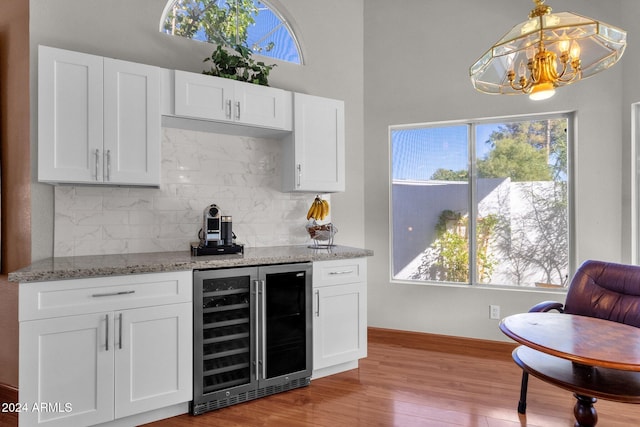 kitchen featuring white cabinets, hanging light fixtures, beverage cooler, light wood-type flooring, and light stone counters