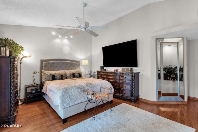 bedroom with a textured ceiling, ceiling fan, wood-type flooring, and vaulted ceiling