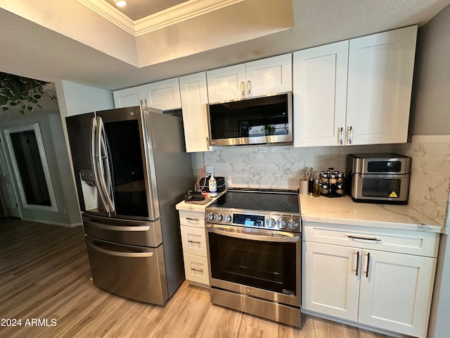 kitchen featuring white cabinets, backsplash, appliances with stainless steel finishes, ornamental molding, and light hardwood / wood-style floors