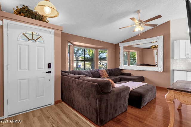 living room with a textured ceiling, vaulted ceiling, light wood-type flooring, and ceiling fan