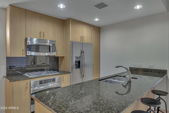 kitchen featuring sink, a kitchen bar, stainless steel appliances, and dark stone countertops