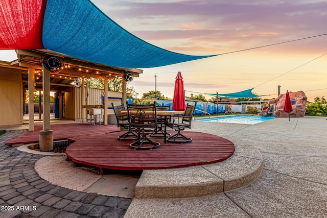 patio terrace at dusk featuring a fenced in pool, outdoor dining area, fence, and a deck