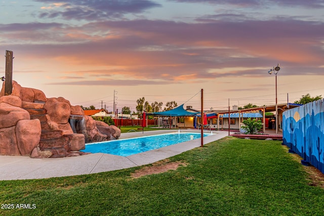 pool at dusk featuring a lawn, fence, an outdoor pool, and a patio