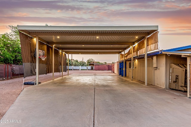 parking at dusk featuring driveway, fence, and an attached carport