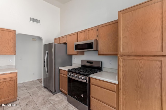 kitchen with light countertops, stainless steel appliances, marble finish floor, a towering ceiling, and visible vents