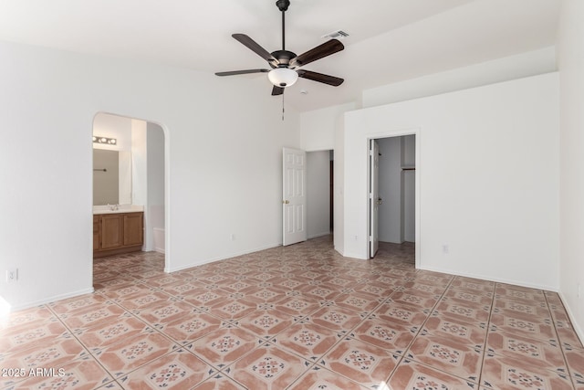 unfurnished bedroom with a sink, a walk in closet, lofted ceiling, visible vents, and arched walkways
