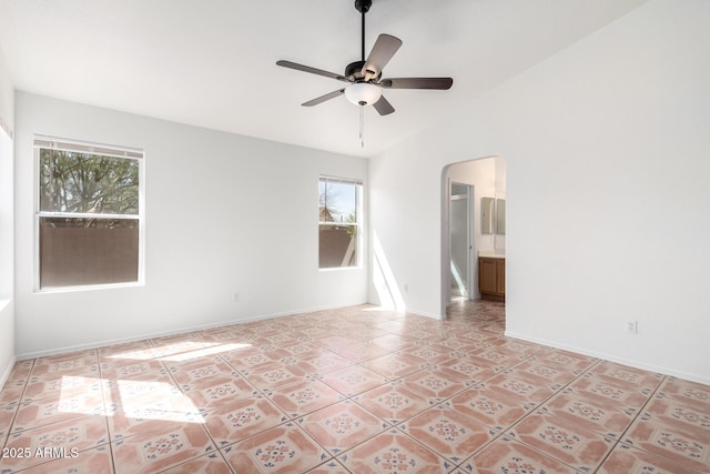 unfurnished room featuring lofted ceiling, light tile patterned floors, baseboards, arched walkways, and ceiling fan