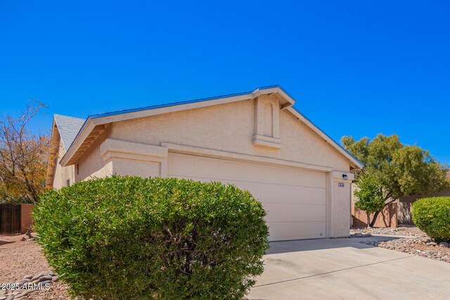 view of home's exterior with stucco siding, driveway, a garage, and fence