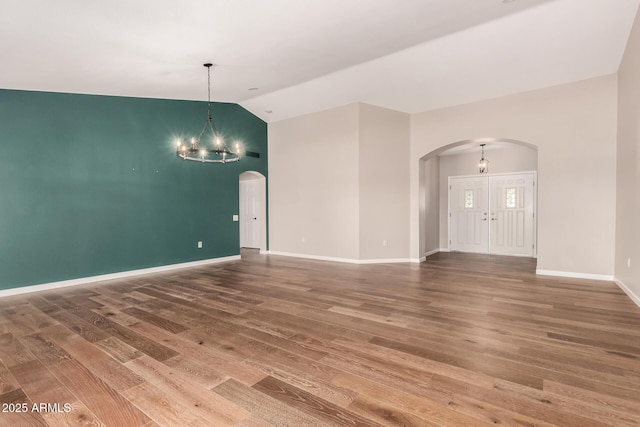 spare room with arched walkways, a chandelier, wood finished floors, baseboards, and vaulted ceiling