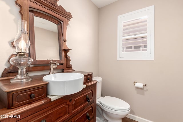 half bath with baseboards, vanity, and toilet