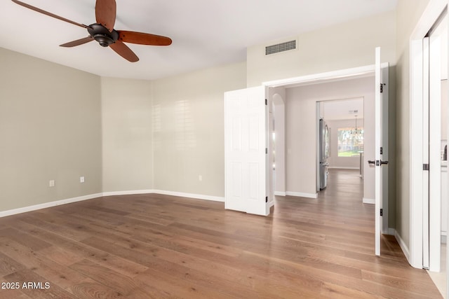 empty room featuring light wood finished floors, a ceiling fan, visible vents, and baseboards