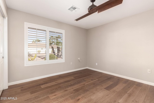 empty room featuring dark wood-style flooring, visible vents, and baseboards