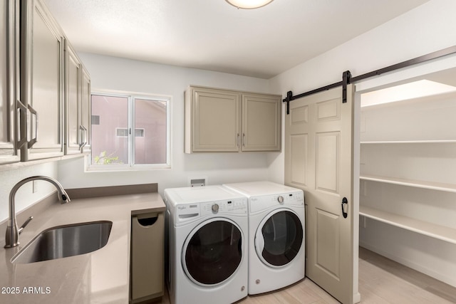 clothes washing area with a barn door, a sink, light wood-type flooring, cabinet space, and washer and clothes dryer