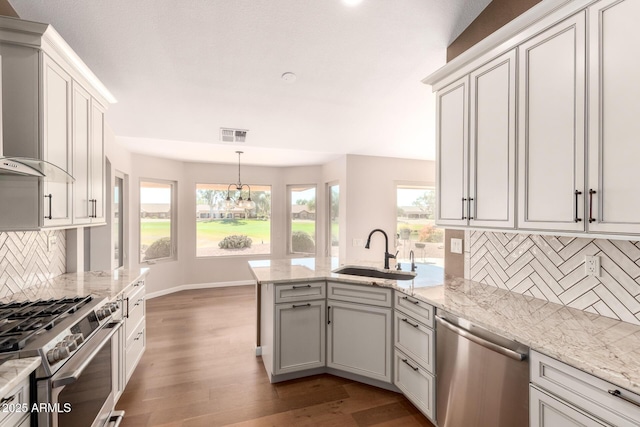 kitchen with light wood-style flooring, a peninsula, stainless steel appliances, wall chimney range hood, and a sink