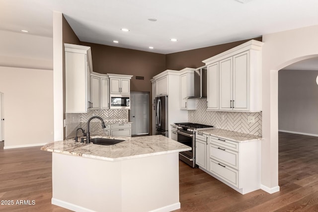 kitchen featuring arched walkways, stainless steel appliances, a peninsula, a sink, and wall chimney exhaust hood