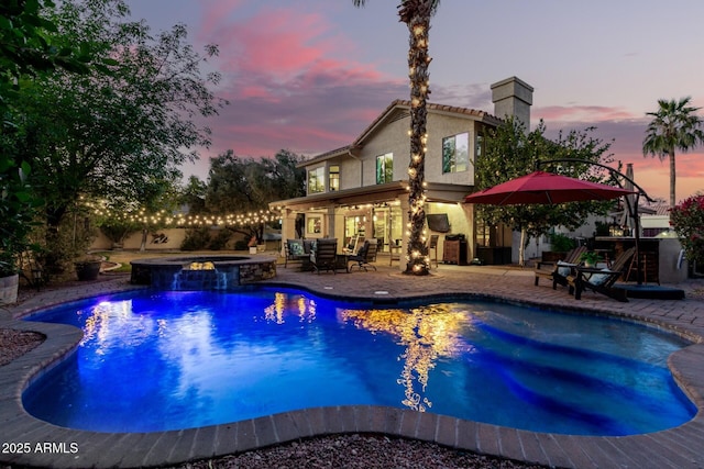 pool at dusk featuring an in ground hot tub and a patio