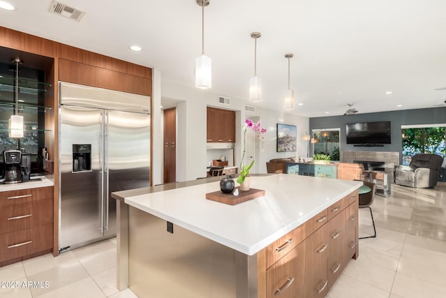 kitchen featuring light tile patterned flooring, a kitchen island, decorative light fixtures, a breakfast bar area, and stainless steel built in fridge