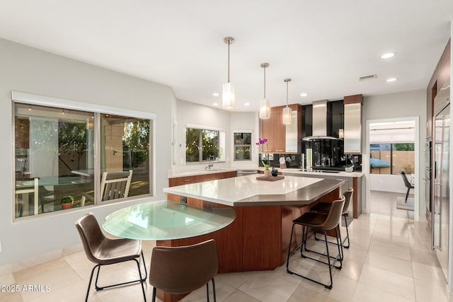 kitchen with wall chimney exhaust hood, a center island, hanging light fixtures, and backsplash