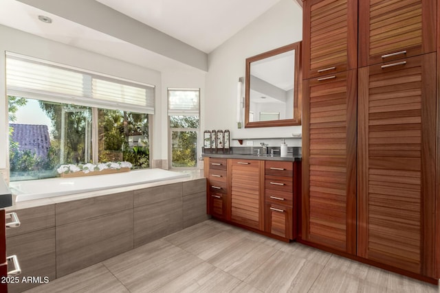 bathroom featuring vanity, lofted ceiling, a healthy amount of sunlight, and a relaxing tiled tub