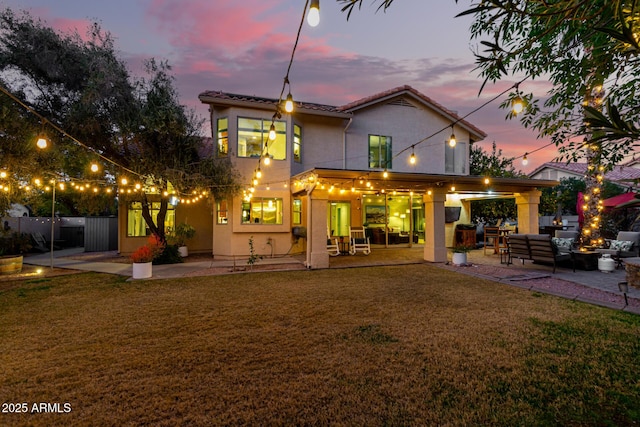 back house at dusk with an outdoor living space, a patio, and a lawn