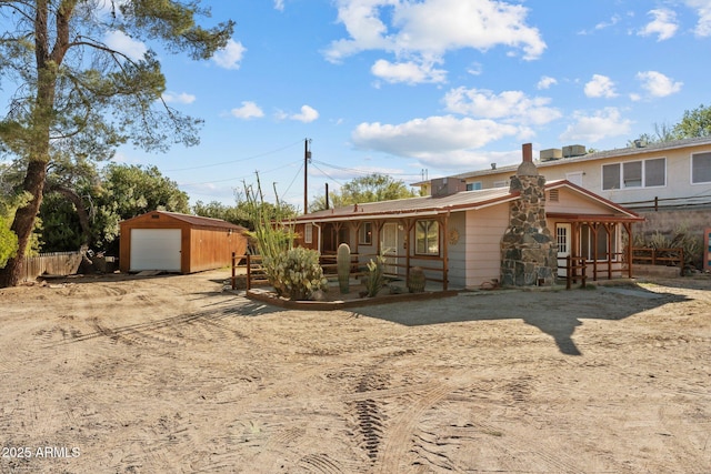 rear view of property with an outdoor structure, covered porch, fence, driveway, and a detached garage