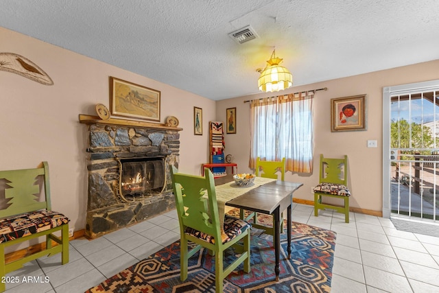 dining area with light tile patterned flooring, visible vents, a stone fireplace, and baseboards