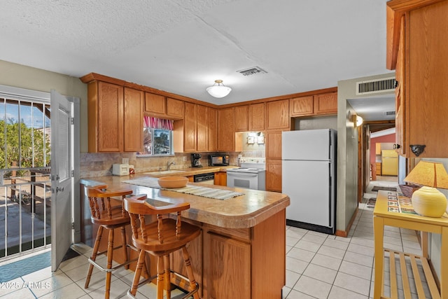 kitchen featuring white appliances, light tile patterned floors, light countertops, visible vents, and a peninsula