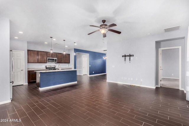 kitchen with appliances with stainless steel finishes, dark hardwood / wood-style flooring, dark brown cabinetry, a kitchen island with sink, and hanging light fixtures