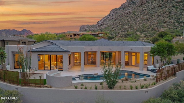 back of house at dusk with a patio, a mountain view, stucco siding, and an in ground hot tub