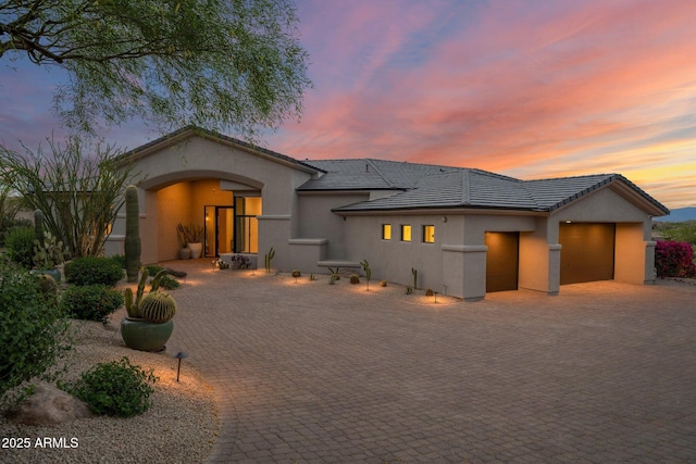 rear view of house with a tile roof, an attached garage, decorative driveway, and stucco siding