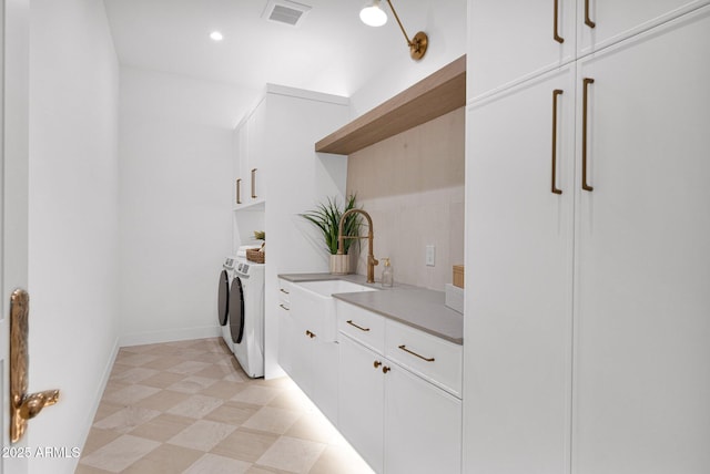 laundry room with washing machine and dryer, visible vents, cabinet space, light floors, and a sink