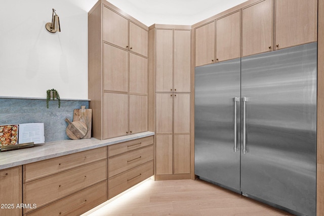 kitchen featuring light stone countertops, light wood-style floors, light brown cabinets, and stainless steel built in refrigerator