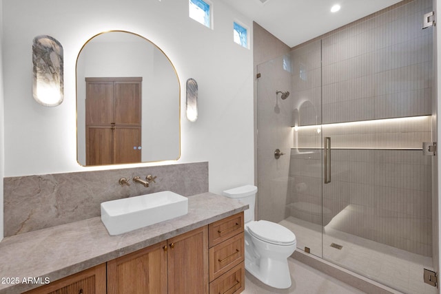 bathroom featuring tasteful backsplash, vanity, a tile shower, and toilet