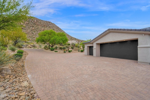 exterior space featuring a mountain view, a garage, decorative driveway, and stucco siding