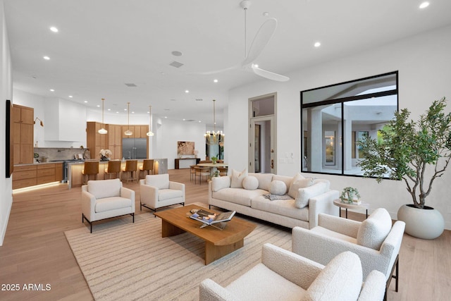 living area with visible vents, light wood-type flooring, recessed lighting, and ceiling fan with notable chandelier