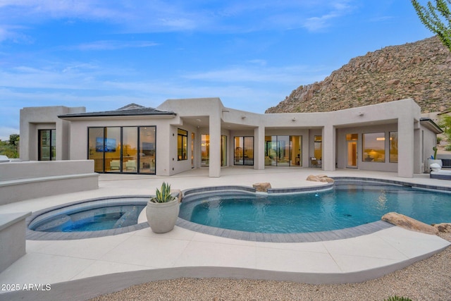 back of house featuring stucco siding, a patio, an in ground hot tub, an outdoor pool, and a mountain view