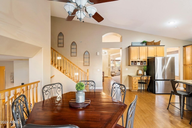 dining room featuring light wood-style flooring, a ceiling fan, high vaulted ceiling, baseboards, and stairs